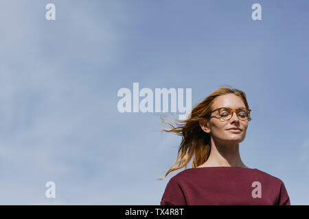 Porträt der jungen Frau mit Brille und geschlossenen Augen unter blauem Himmel Stockfoto