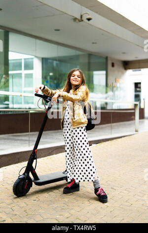 Portrait von lächelnden Mädchen mit E-Scooter tragen goldene Pailletten Jackett und Polka Dot jumpsuit Stockfoto