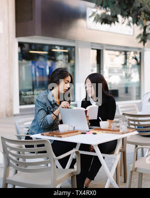 Zwei Freunde sitzen zusammen in einem Cafe mit Buch und Laptop Stockfoto