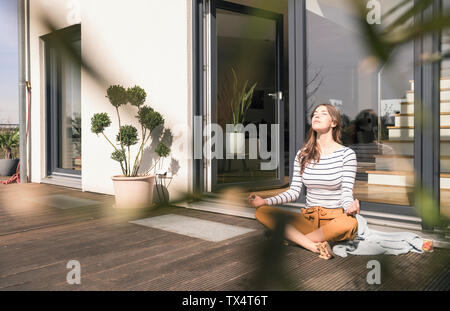 Junge Frau sitzt auf der Terrasse zu Hause üben Yoga Stockfoto