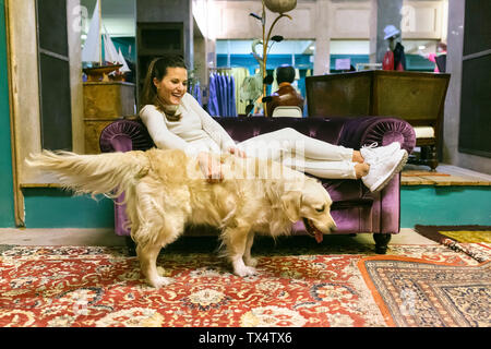 Lächelnde Frau mit Hund liegend auf der Couch in einem Vintage Shop Stockfoto