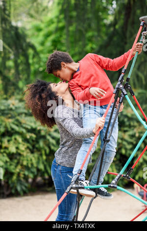 Mutter und Sohn spielen auf dem Spielplatz im Park, klettern in einem Jungle Gym Stockfoto