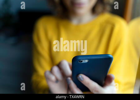 Frau in einem gelben Pullover, mit Smartphone Stockfoto