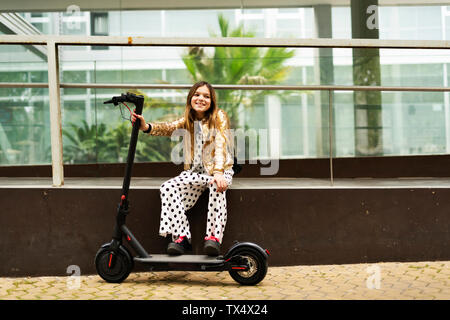 Portrait von lächelnden Mädchen mit E-Scooter tragen goldene Pailletten Jackett und Polka Dot jumpsuit Stockfoto