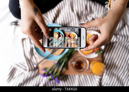 Frau sitzt auf dem Bett, unter Smartphone Bilder von Ihr haelthy Frühstück Stockfoto