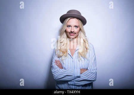 Porträt der blonde junge Frau mit gefälschten Schnurrbart und Hut crossing Arms Stockfoto