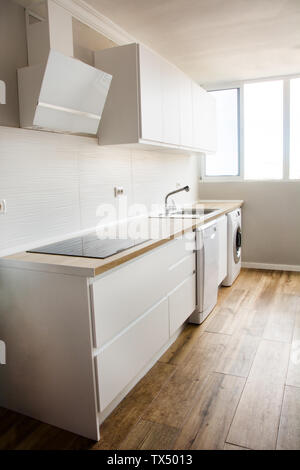 Weiße, moderne Küche mit weißen Möbeln und Holzboden Stockfoto