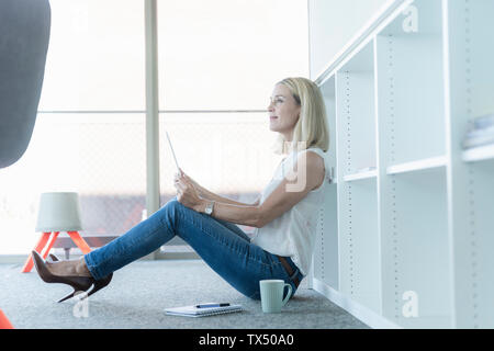 Casual Geschäftsfrau, sitzen auf dem Boden im Büro mit Tablet Stockfoto