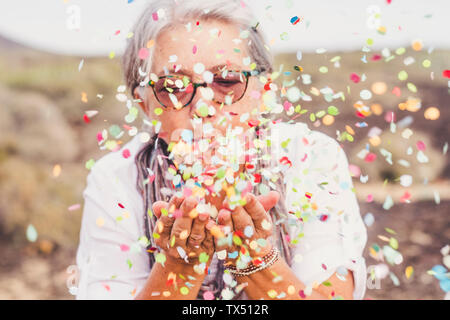 Ältere Frau blasen Konfetti im Freien Stockfoto