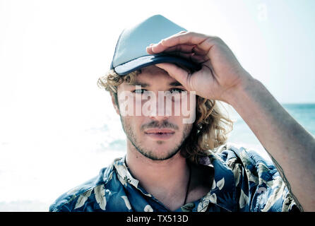 Portrait von bärtigen blonden Mann, der Baseball Cap vor dem Meer Stockfoto