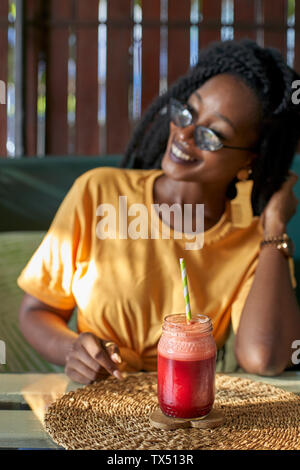 Lächelnde junge Frau mit Dreadlocks in einen Smoothie in einem Cafe Stockfoto