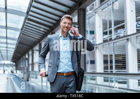 Lächelnd Geschäftsmann mit Gepäck und Handy auf fahrsteig Stockfoto