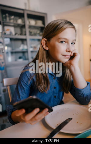 Portrait von Mädchen zu Hause sitzen am Tisch mit Handy Stockfoto