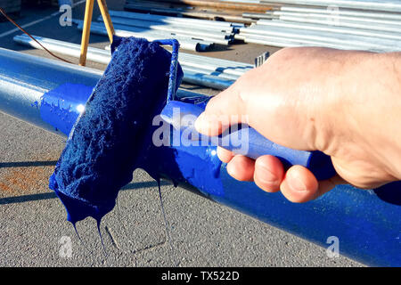 Arbeitnehmer Farben Stahlrohr mit Rolle, um Rost zu verhindern. Blaue Farbe Stockfoto