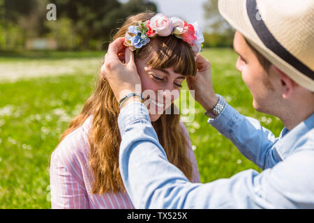 Junger Mann Blumen setzen auf auf den Kopf seiner Freundin Stockfoto