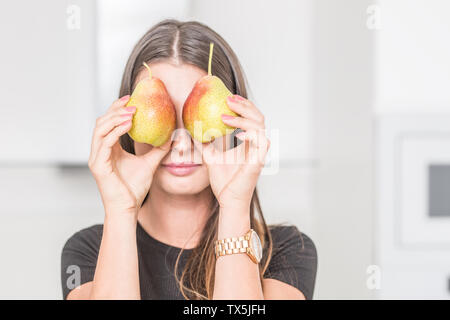 Junge Frau in der Küche zu Hause über zwei Birnen. Stockfoto