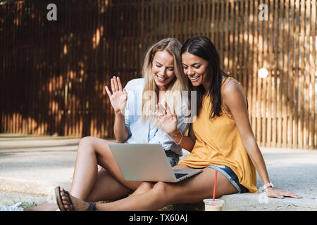 Zwei lächelnde junge Mädchen mit Laptop im Park, Lachen, Plaudern Stockfoto