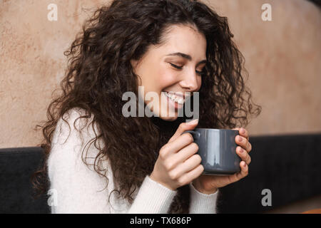 Bild von ziemlich glücklich Mädchen im Cafe Kaffee trinken Holding Schale sitzen. Stockfoto
