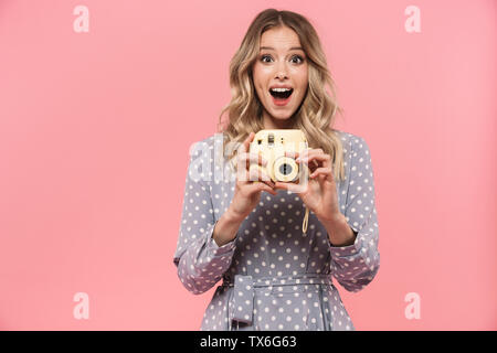 Portrait von eine wunderschöne blonde junge Frau Sommer Kleid stehen über rosa Hintergrund isoliert, mit Instant Foto Kamera Stockfoto