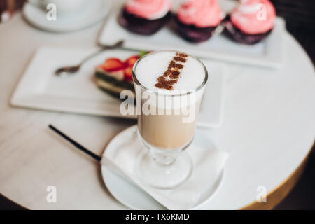 Leckeren Latte in Glas Couchtisch mit Cupcakes. Stockfoto