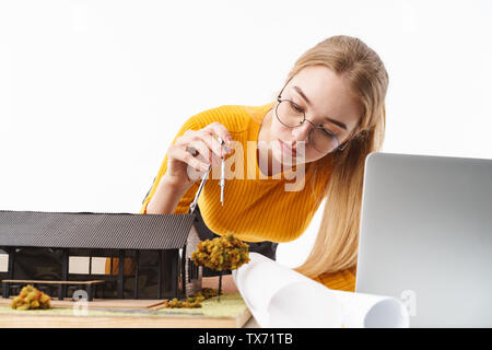 Schöne junge blonde Frau, Architekt, die auf weißem Hintergrund, auf ein neues Projekt an einem Schreibtisch mit Laptop arbeiten Stockfoto