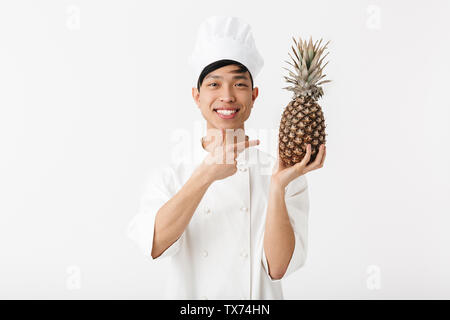 Asiatische Koch tragen Uniform, die auf weißem Hintergrund aufgeregt, Ananas angezeigt Stockfoto