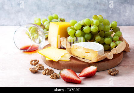 Verschiedene Käsesorten mit Erdbeeren und Trauben auf einem Holzbrett closeup Stockfoto