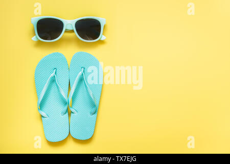 Blue Sun Gläser und Strand flip flops auf druckvolle gelben Hintergrund. Sommer tropische Ferien. Platz für Text. Reisen Urlaub Konzept. Stockfoto