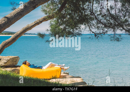 Frau ruht auf gelb Luft Sofa am Strand des Meeres mit blau-transparent Wasser Stockfoto