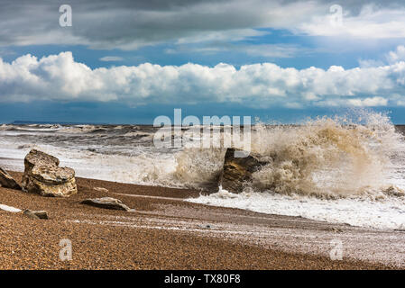 Wellen gegen die Felsen während eines Winters Sturm auf einem Dorset Strand, Landschaft Bild mit einem Moody sky Stockfoto