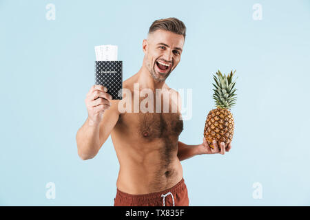 Bild von einem stattlichen aufgeregt Glückliche erwachsene Menschen über die blaue Wand Hintergrund holding Passport und Ananas isoliert posieren. Stockfoto