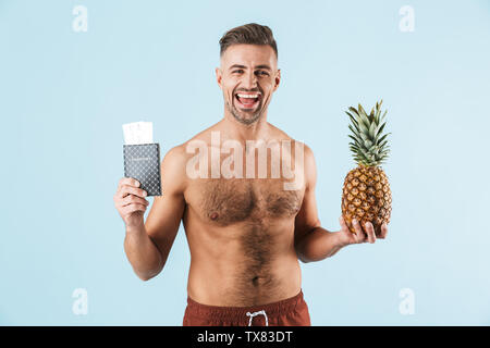 Bild von einem stattlichen aufgeregt Glückliche erwachsene Menschen über die blaue Wand Hintergrund holding Passport und Ananas isoliert posieren. Stockfoto