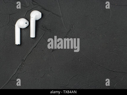 White kabellose Bluetooth® Kopfhörer auf dunklen konkreten Hintergrund, Ansicht von oben Stockfoto