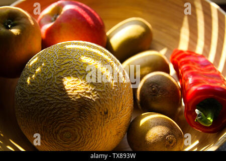 Close up Bambus Obstkorb mit Melone, Äpfel, Kiwis, Paprika von Abendsonne Balken leuchtet auf Stockfoto