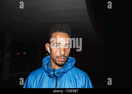Zuversichtlich passen junge afrikanische Sport Mann windbreaker Outdoor Aktivitäten in der Nacht Zeit tragen, trägt drahtlose Kopfhörer Stockfoto