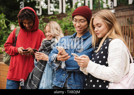Gruppe, wenn Fröhliche multiethnischen Freunde Jugendliche lustige Zeit zusammen im Freien verbringen, stehen, über Mobiltelefone Stockfoto
