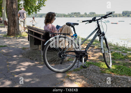 Belgrad, Serbien, 22. Juni 2019: Junge Frau sitzt auf einer Bank neben einem geparkten Fahrräder an der Donau Riverside Promenade in Zemun Stockfoto