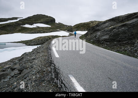 Norwegischer Sicht mit Kerl in eine blaue Jacke in den Bergen. Landschaft in der Nähe der schneebedeckten Straße bjorgavegen, Norwegen. Touristische Route Aurlandsfjellet läuft aus Stockfoto