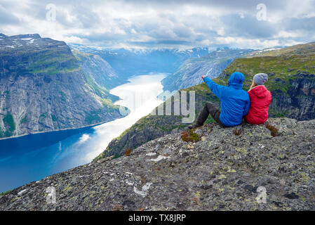 Paar sitzt auf Felsen und blickt auf die Berge in der Nähe von trolltunga. Beliebte Touristenattraktion. Ringedalsvatnet - See in der Gemeinde Odda in Hordalan Stockfoto