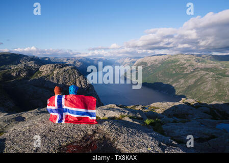 Preikestolen weg. Paar mit der Flagge Norwegens blickt auf das Panorama der Lysefjord. Touristische Attraktion. Sonniges Wetter in den Bergen Stockfoto