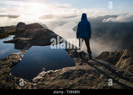 In der Nähe von Preikestolen, der berühmte Touristenattraktion in Ryfylke, ragt über den Lysefjord. Kerl auf einem Felsen in die Ferne schaut und genießt Stockfoto