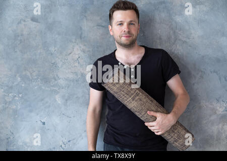 Jungen kaukasischen Mann in Schwarz t-shirt Holding Yoga Matte in der Nähe von Studio Wand Stockfoto