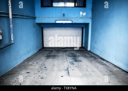 Private Tiefgarage mit weiße Tür und blaue Wände. Parkplatz unter dem Wohnhaus. Stockfoto