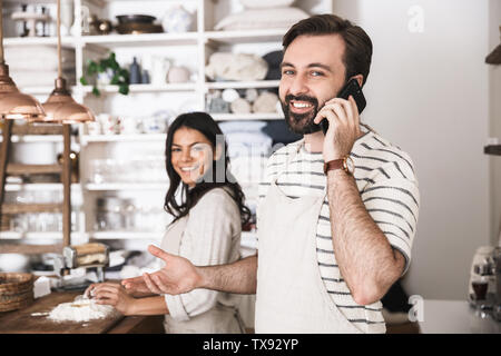 Portrait von zufriedenen Paar Mann und Frau 30 s Schürzen tragen Sie Ihr Smartphone während gemeinsames Kochen in der Küche zu Hause. Stockfoto