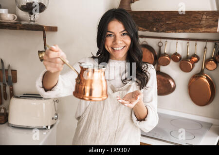 Portrait der Junge brünette Frau 30 s tragen Schürze mit Geschirr zu Hause beim Kochen in der Küche Stockfoto