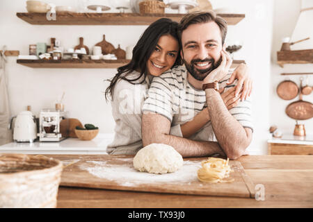 Bild des schönen Familie Mann und Frau 30 s tragen Schürzen, hausgemachte Pasta Teig, während das gemeinsame Kochen in der Küche zu Hause. Stockfoto