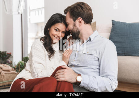 Bild von adorable Paar Mann und Frau zusammen, umarmt, während auf dem Sofa im hellen Zimmer zu Hause sitzen Stockfoto
