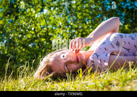 Schöne und junge Mädchen bläst Seifenblasen. Das Mädchen liegt auf dem grünen Rasen vor dem Hintergrund des Waldes. Stockfoto