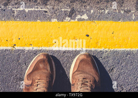 Eine Person steht neben der gelben Linie gezeichnet. Schuhe stoin auf dem Bürgersteig Grauton. Stockfoto
