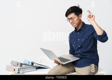 Foto der fokussierten asiatischer Mann 30 s tragen Brillen Daumen und mit Laptop, während in hellen Büro Raum arbeiten Stockfoto